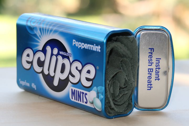 a rolled up strip of green cotton placed into an empty tin of Eclipse mints