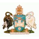 A shield shows a crossed sword and mace, a three towered castle and the rose of York. Atop is a wreath on which sits a crowned portcullis. A gum tree is behind the portcullis. The shield is supported by two swans. One black and one white.